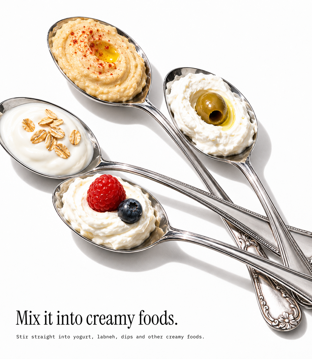Four silver spoons arranged diagonally on a white background, each holding a creamy food topping: hummus with olive oil and paprika, yogurt with oats, whipped cream with a raspberry and blueberry, and whipped cream with an olive. Text at the bottom reads, 'Mix it into creamy foods.
