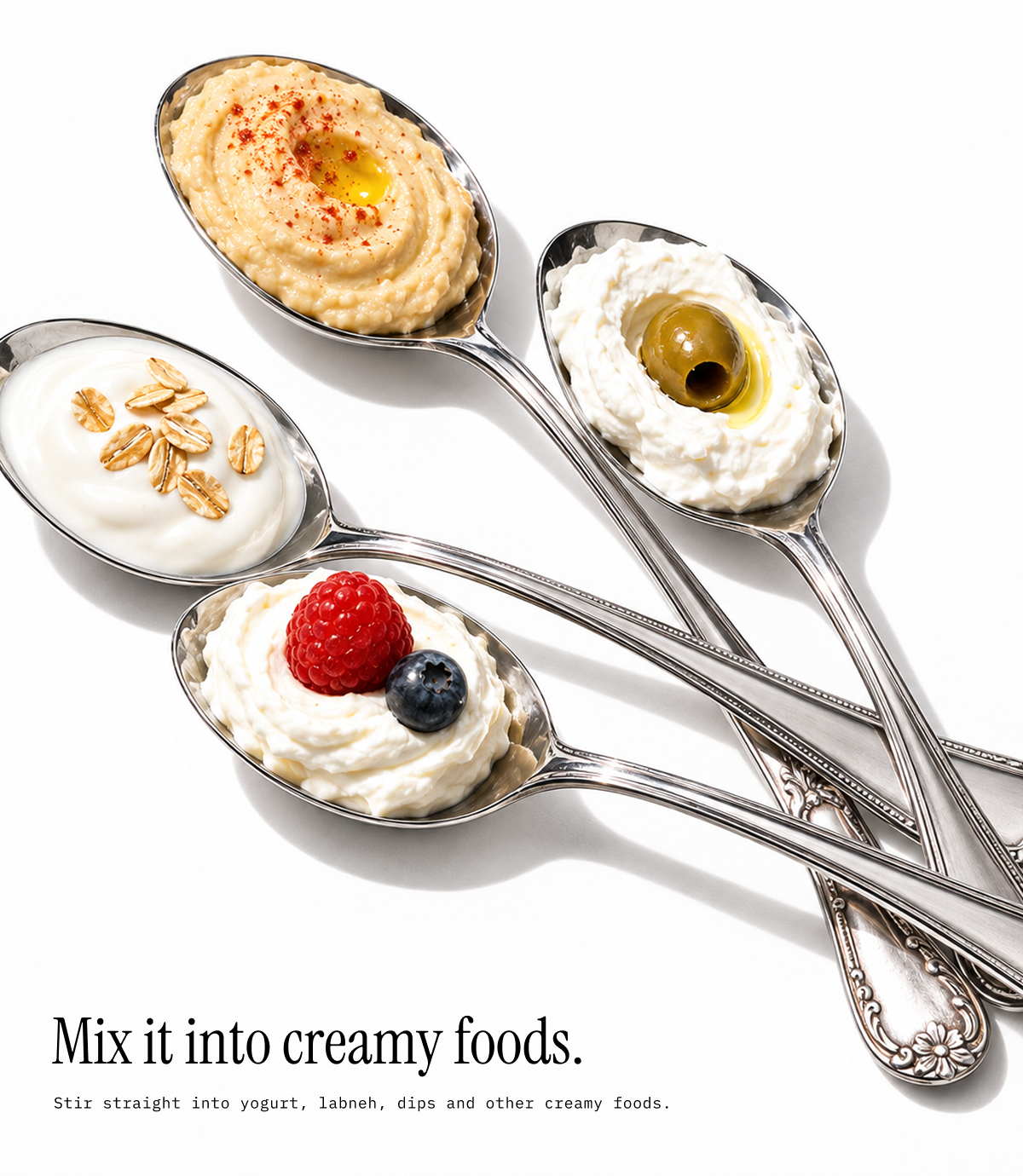 Four silver spoons arranged diagonally on a white background, each holding a creamy food topping: hummus with olive oil and paprika, yogurt with oats, whipped cream with a raspberry and blueberry, and whipped cream with an olive. Text at the bottom reads, 'Mix it into creamy foods.