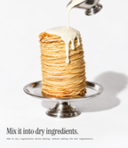 A tall stack of golden pancakes on a silver pedestal plate, with white syrup being poured from a metal pitcher. Text at the bottom reads, 'Mix it into dry ingredients.