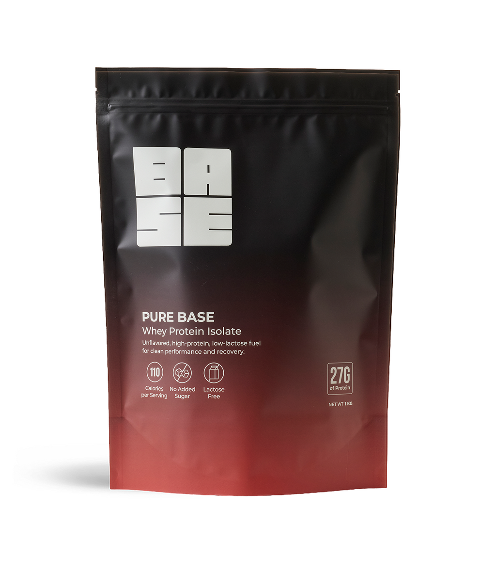A stand-up pouch of Pure Base Whey Protein Isolate powder, featuring a black-to-red gradient design with a white logo and product details on a clean white background.