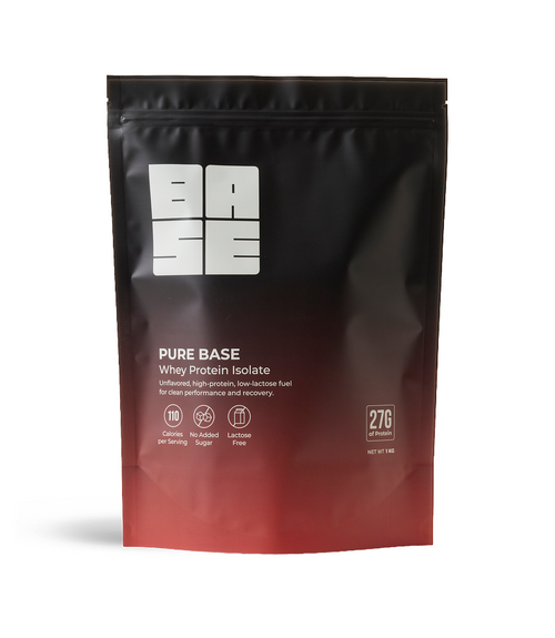 A stand-up pouch of Pure Base Whey Protein Isolate powder, featuring a black-to-red gradient design with a white logo and product details on a clean white background.