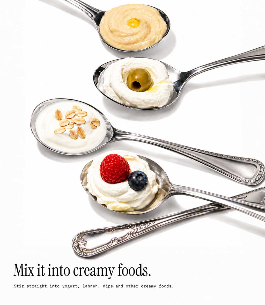 Four silver spoons arranged diagonally on a white background, each holding a different creamy food topping: hummus, yogurt with an olive, yogurt with nuts, and whipped cream with a raspberry and blueberry. Text at the bottom reads, 'Mix it into creamy foods.