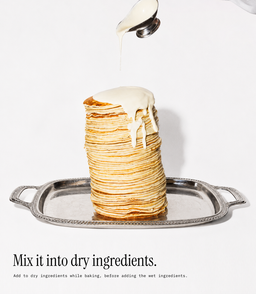 A tall stack of golden pancakes on a silver tray, with white syrup being drizzled from a spoon over the top. Text at the bottom reads, 'Mix it into dry ingredients.
